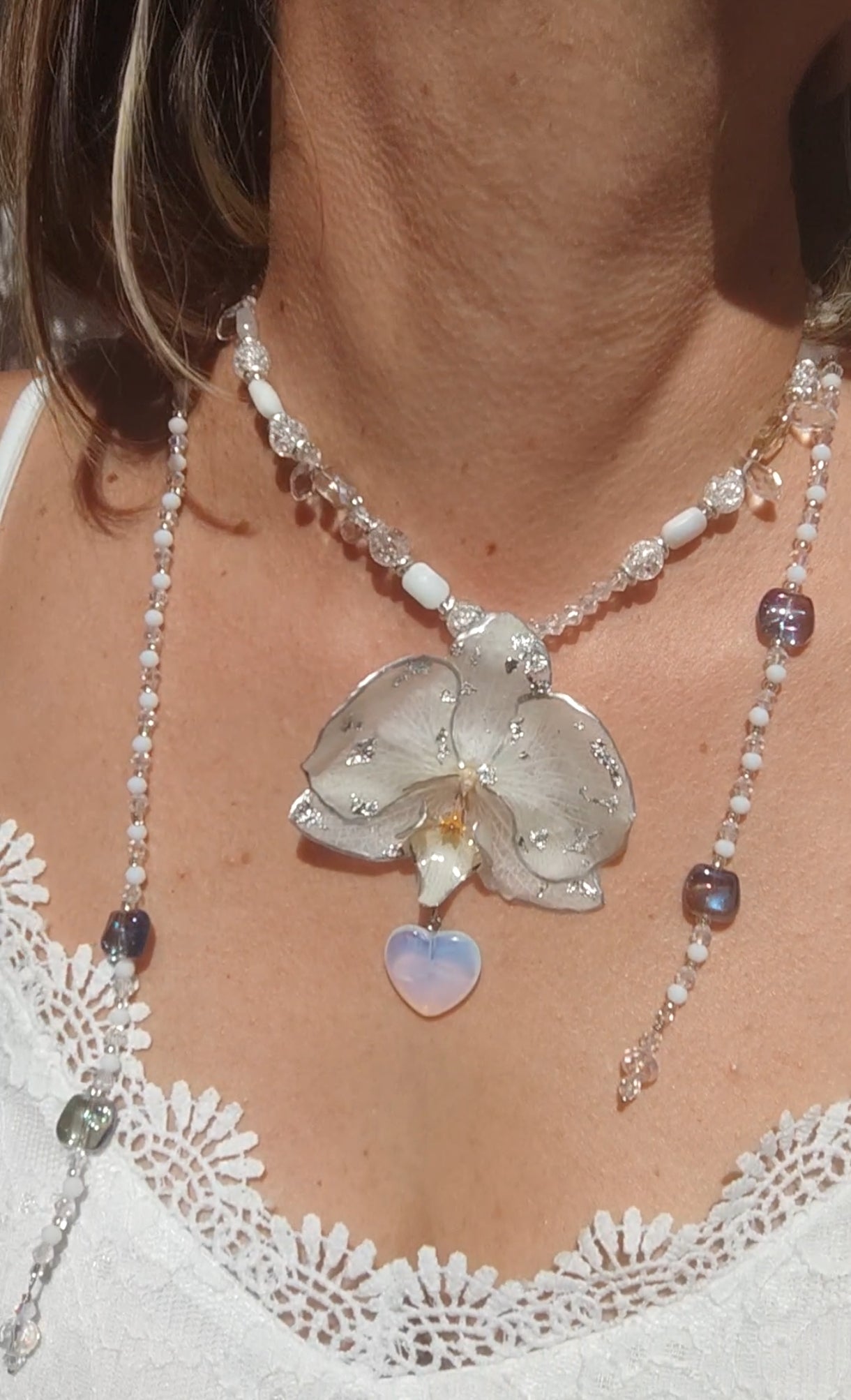 Collar largo hecho a mano con orquídea real blanca resinada, detalles plateados y corazón de piedra luna