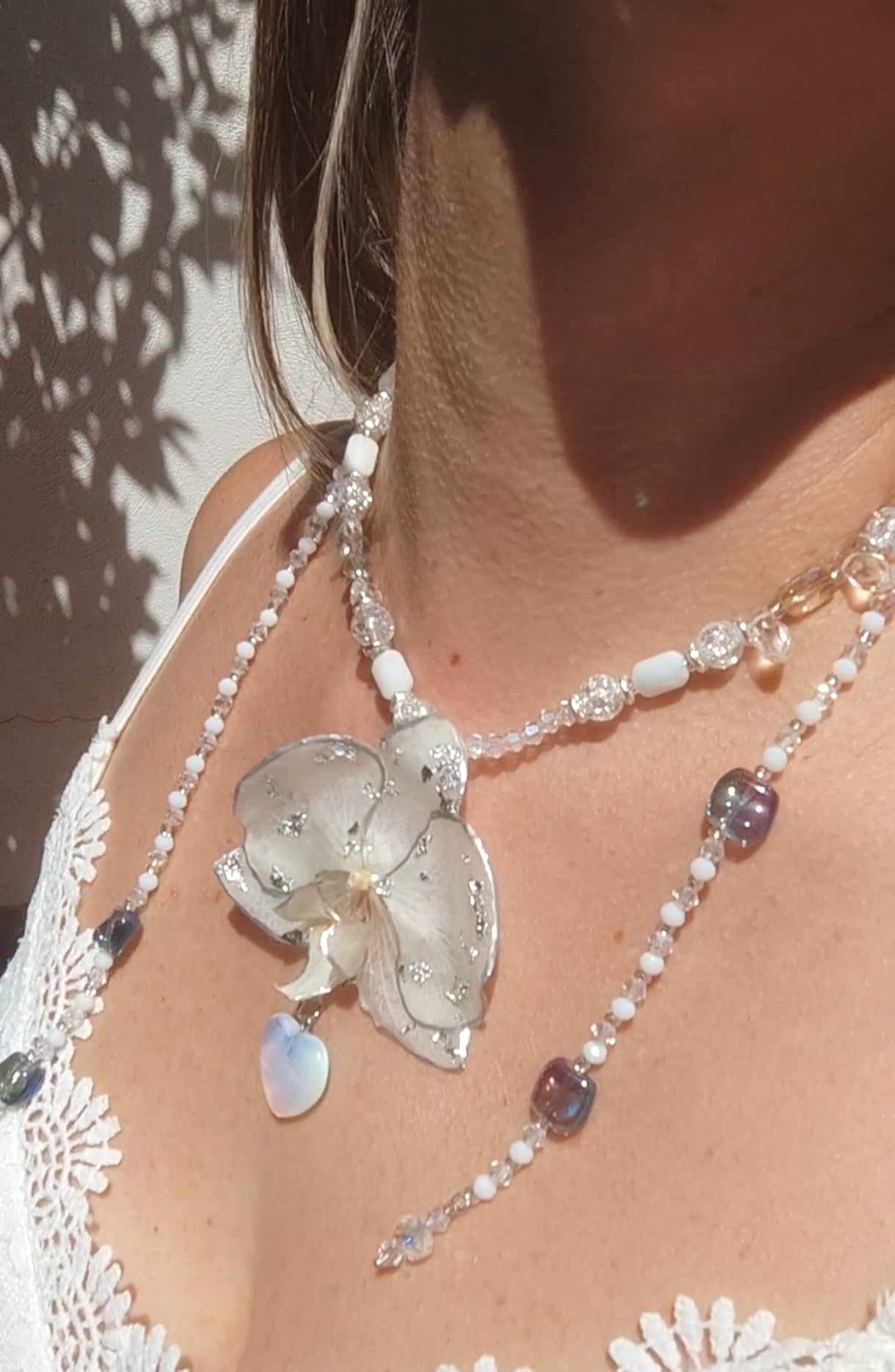 Collar largo hecho a mano con orquídea real blanca resinada, detalles plateados y corazón de piedra luna