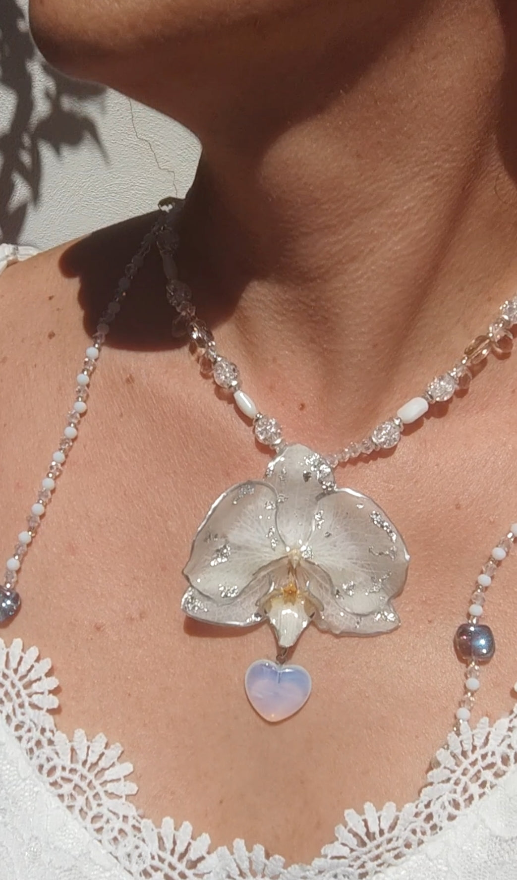 Collar largo hecho a mano con orquídea real blanca resinada, detalles plateados y corazón de piedra luna
