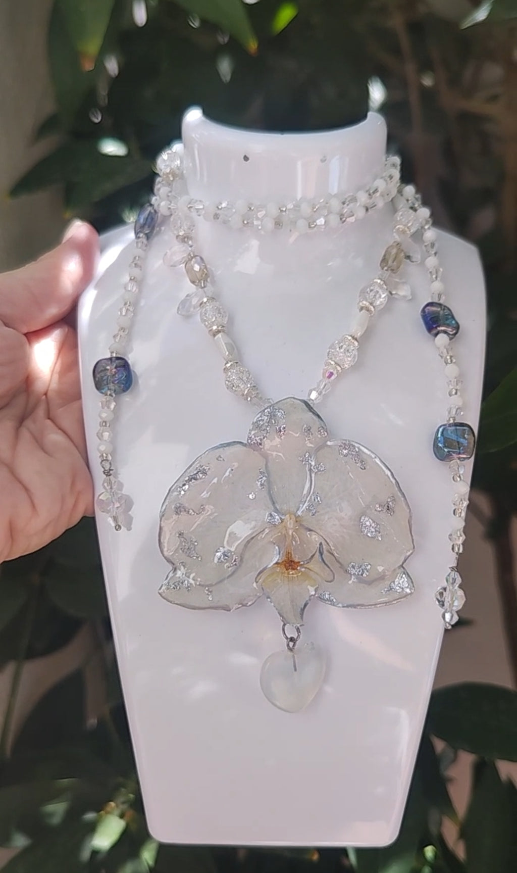 Collar largo hecho a mano con orquídea real blanca resinada, detalles plateados y corazón de piedra luna