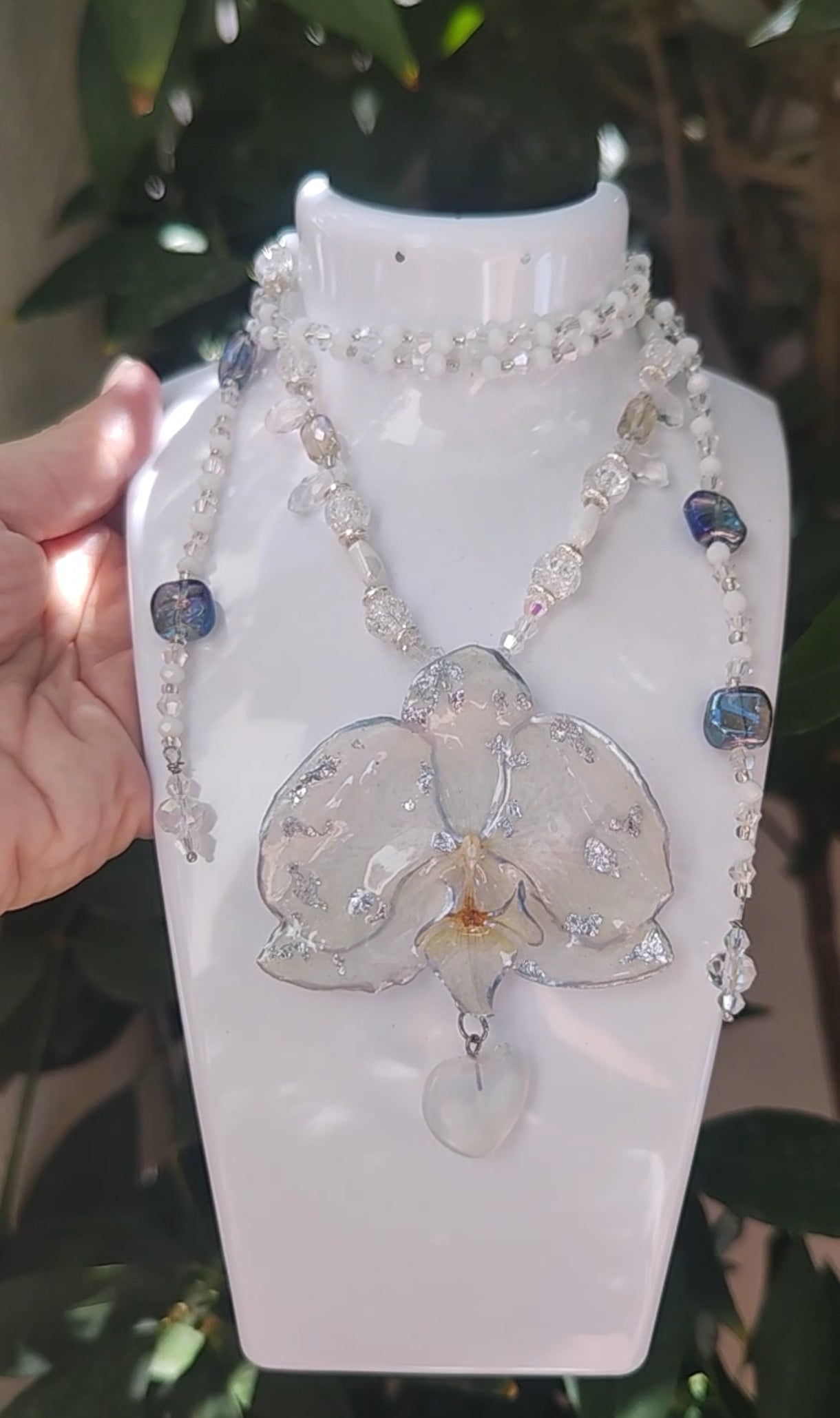 Collar largo hecho a mano con orquídea real blanca resinada, detalles plateados y corazón de piedra luna