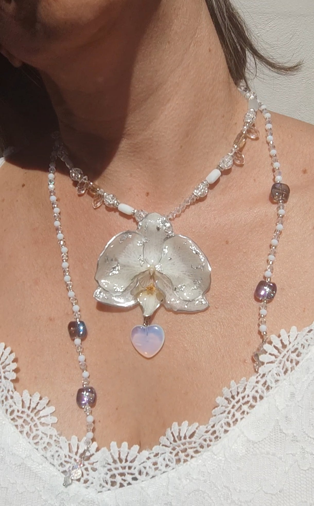 Collar largo hecho a mano con orquídea real blanca resinada, detalles plateados y corazón de piedra luna