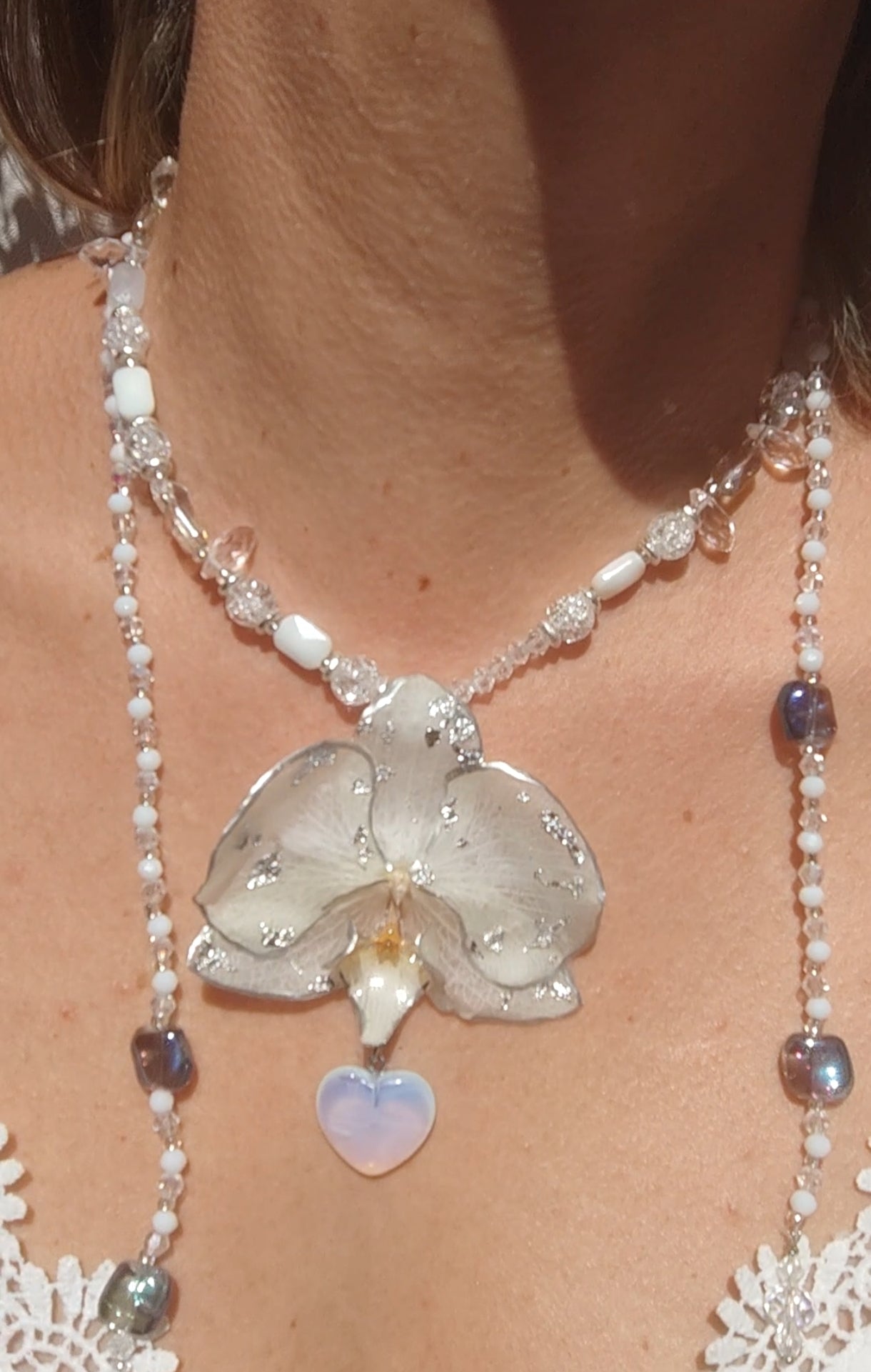 Collar largo hecho a mano con orquídea real blanca resinada, detalles plateados y corazón de piedra luna