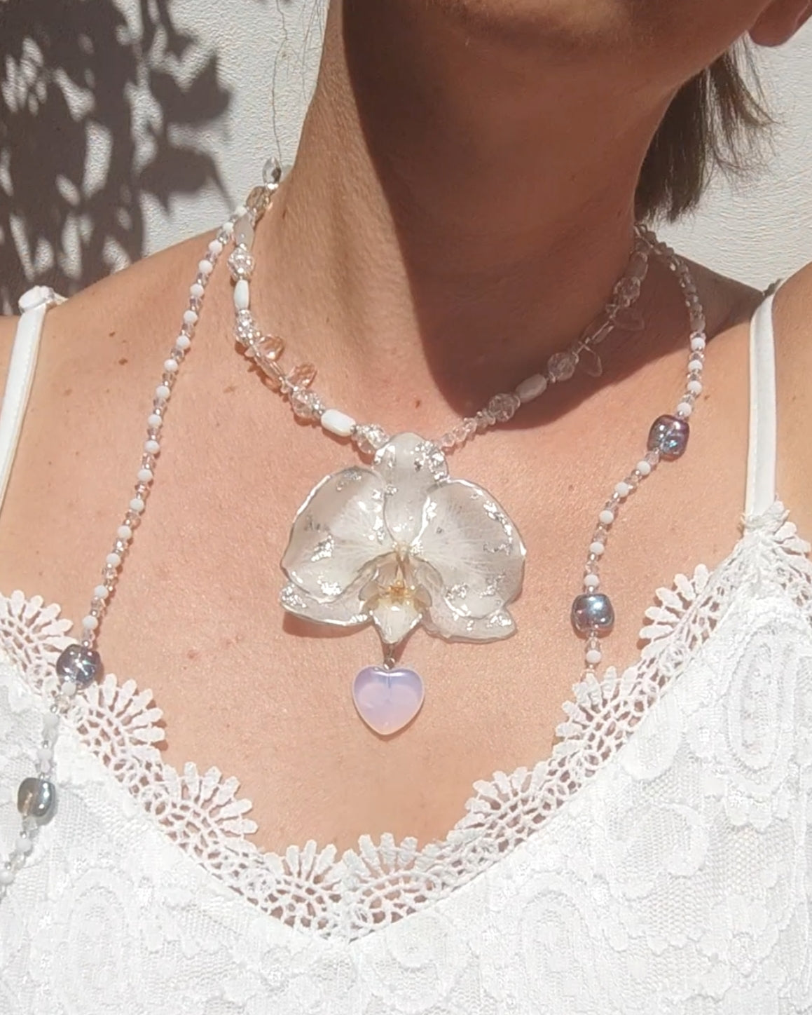 Collar largo hecho a mano con orquídea real blanca resinada, detalles plateados y corazón de piedra luna