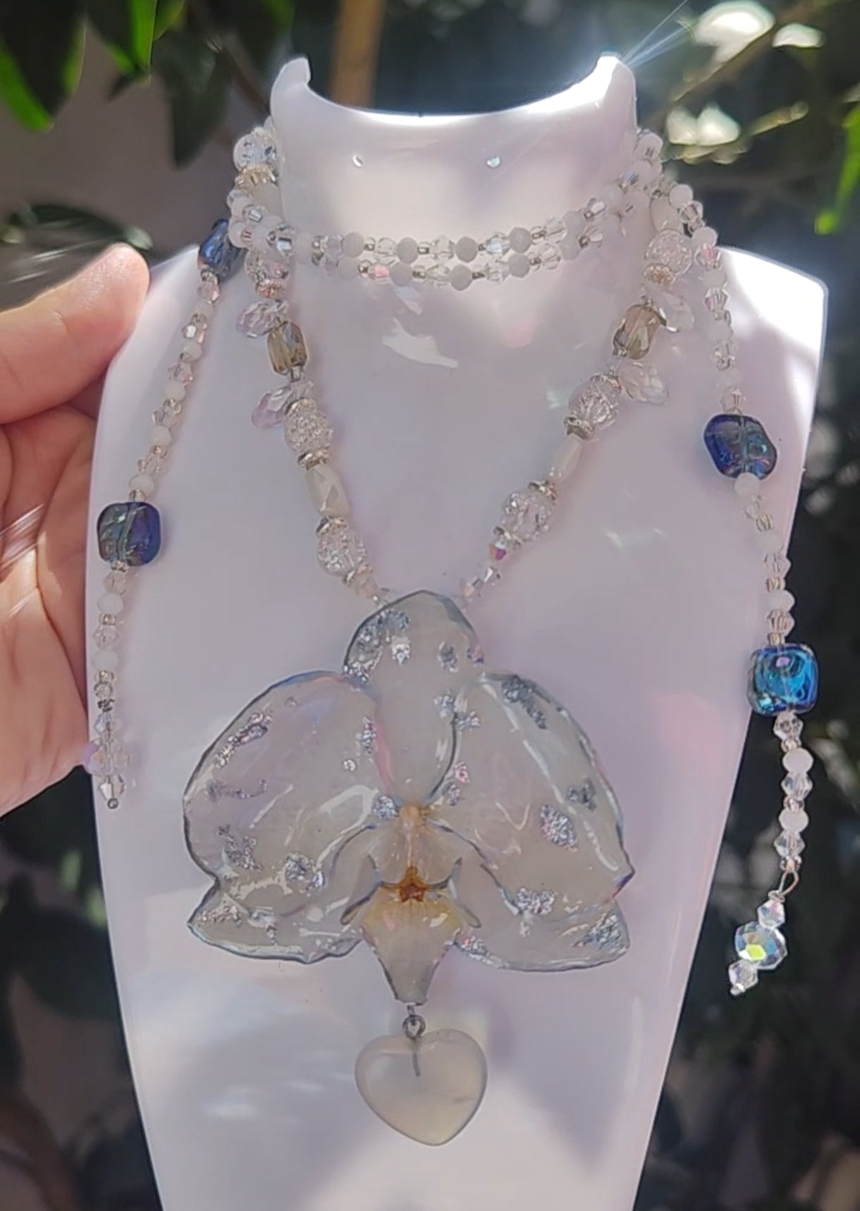 Collar largo hecho a mano con orquídea real blanca resinada, detalles plateados y corazón de piedra luna