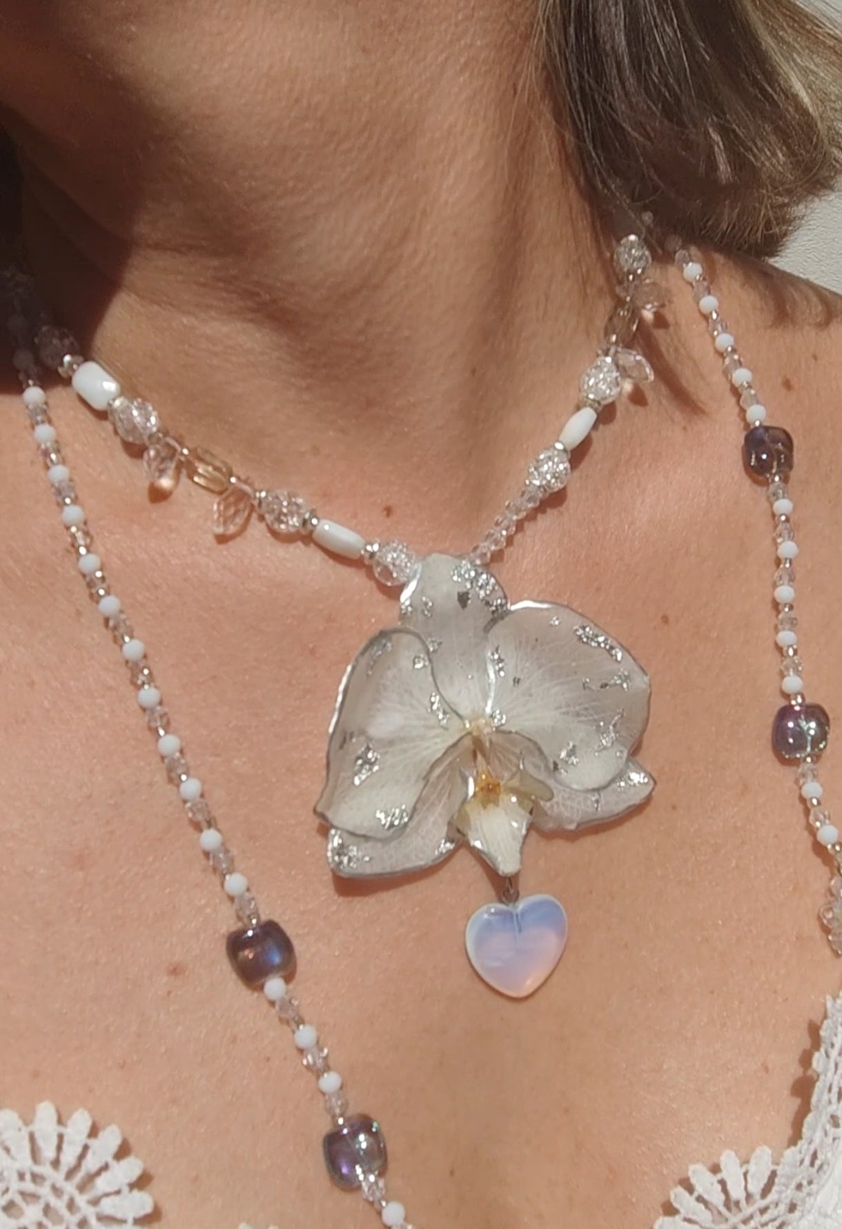 Collar largo hecho a mano con orquídea real blanca resinada, detalles plateados y corazón de piedra luna