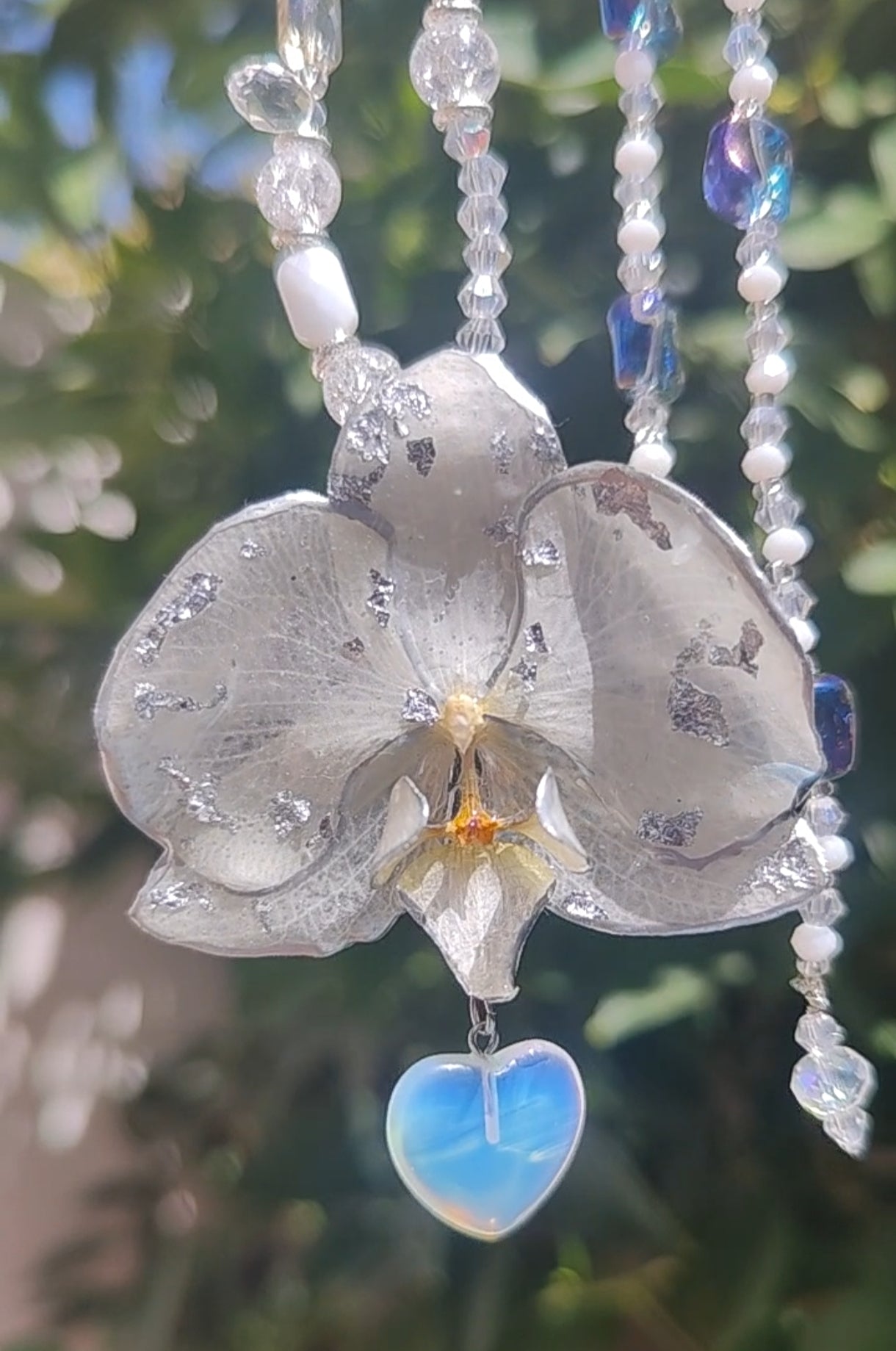 Collar largo hecho a mano con orquídea real blanca resinada, detalles plateados y corazón de piedra luna